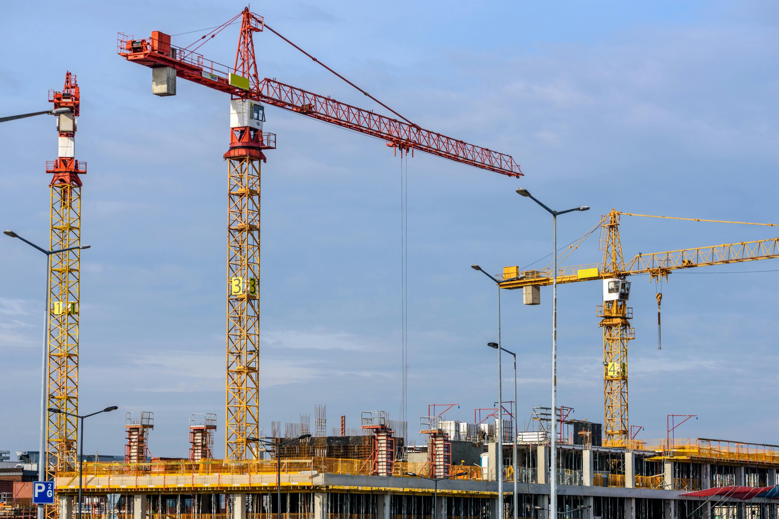 Multiple tower cranes working on a large construction site with blue sky backdrop.