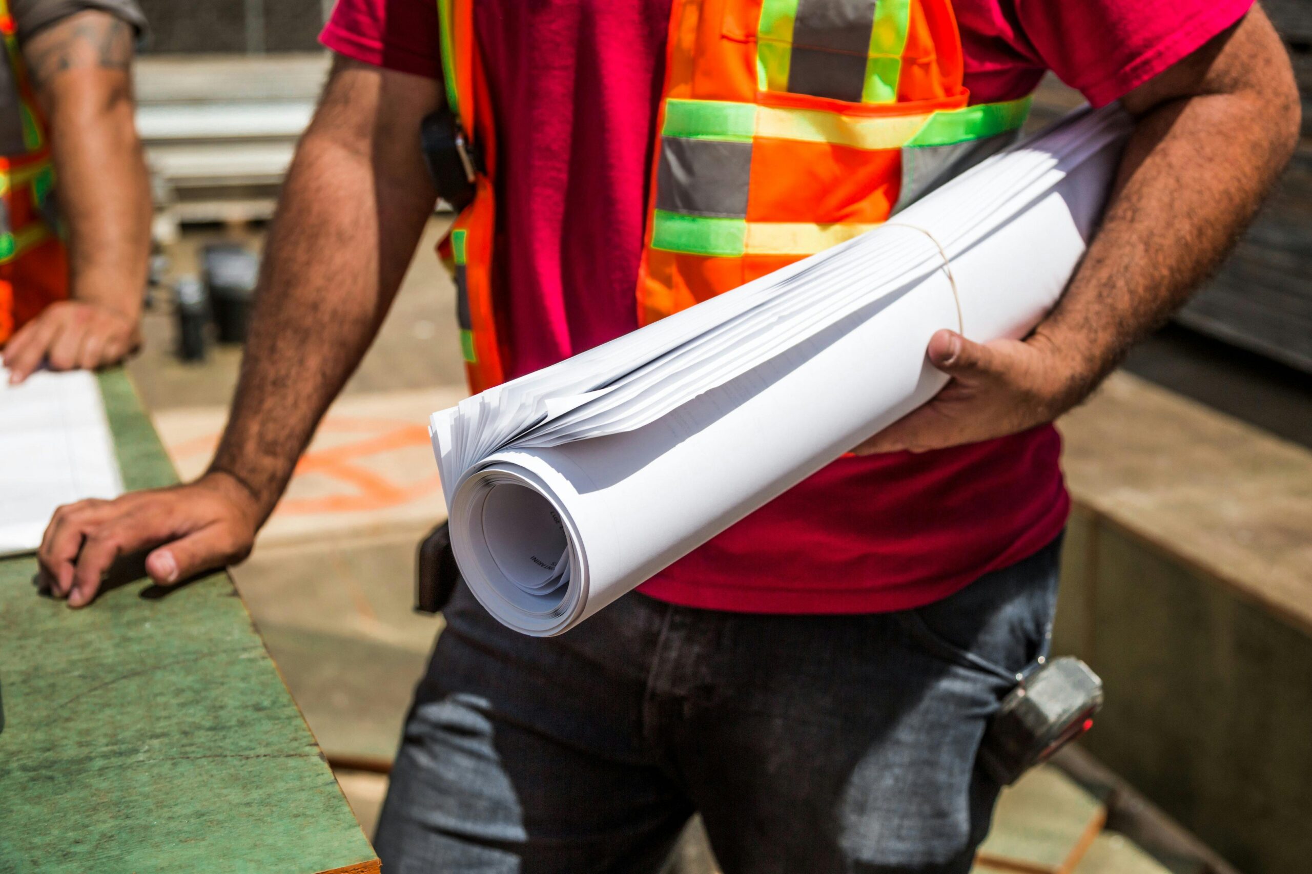 Construction workers in safety vests holding blueprints at a site during the day.